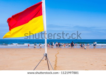 Red and yellow lifeguard safety flag on a beach in the north east of England with families and children playing in the sea in the backgrond