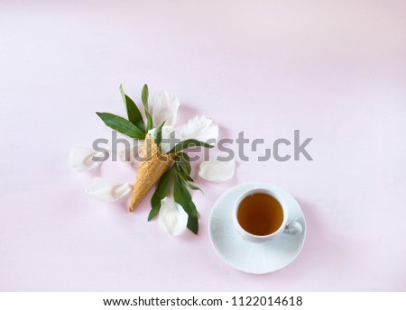 on a pink background a peony flower in a cone for ice cream, a cup of tea