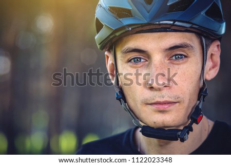 Man cyclist is wearing a sports gray helmet on his head in the background of green nature. The concept of mandatory protection during Cycling