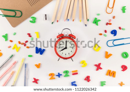 Creative flat lay back to school concept with alarm clock, color school and office supplies on white table background with copy space, frame, template for text or design