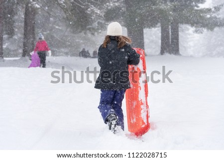 Young girl running up toboggan hill carrying her sled, Canada.