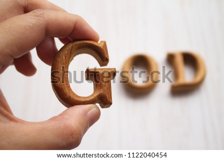Hand holding an alphabet "G" which made of teak wood while another characters left behind. The whole composition can be read as a word 'god'.