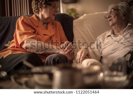 Close up of two elderly woman sitting on sofa and talking .