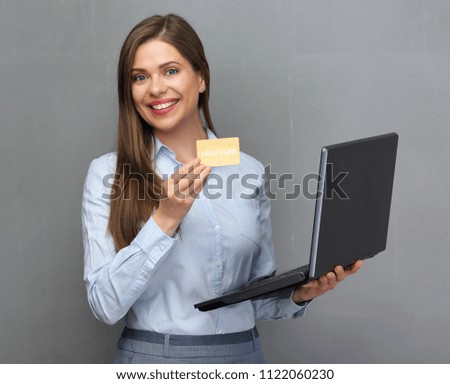 Smiling woman bank employee holding open laptop and gold credit card. Gray wall back isolated.