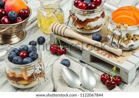 Blueberry, cherry and apricot parfaits in mason jars, on a rustic wood background. Healthy still life concept food. Yogurt and fresh summer fruits parfait 