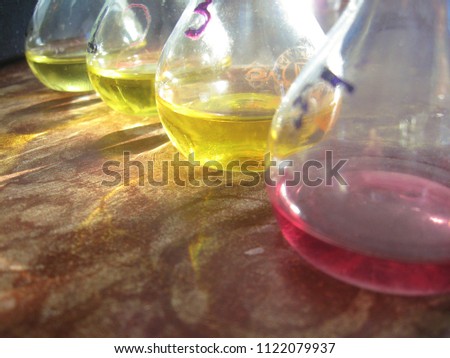 A raw of measuring flasks filled with yellow and red liquid. Old-stile chemical lab interior. The light shines in the flasks and reflects on a table surface. Still-life.