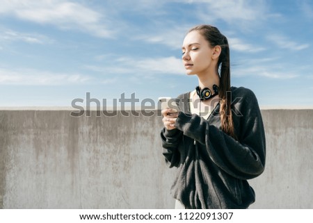 beautiful athletic girl in black sportswear resting after training in the sun, holding a smartphone