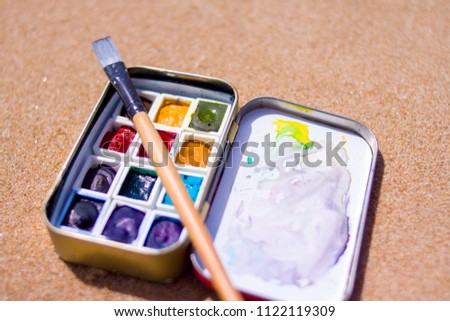 creation, drawing and freedom concept - Artistic equipment: paint brushes, watercolors paintings on sand background at sunny summer day