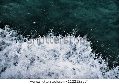 Dark blue ocean water with splashing wave and white air foam bubble. This is texture background for designers. Image has grain or blurry or noise and soft focus when view at full resolution.