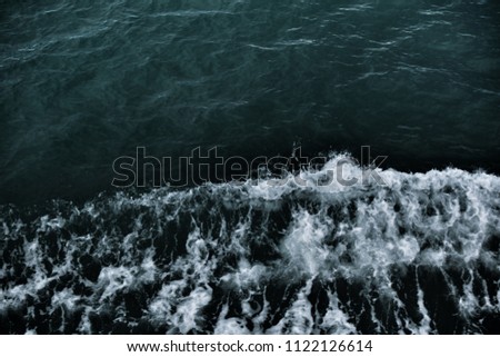 Dark blue ocean water with splashing wave and white air foam bubble. This is texture background and free space for designers. Image has grain or blurry or noise and soft focus.