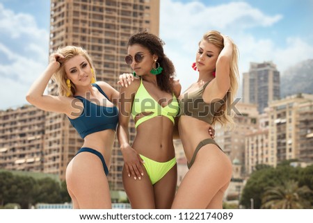 Portrait of young female friends having fun on the sea shore. Pretty women wearing bikini swimsuits. Summer holidays and vacation concept.
