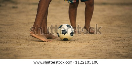 Kids are playing soccer football with bare foot on the dirt in the sunshine day. Picture with space area.