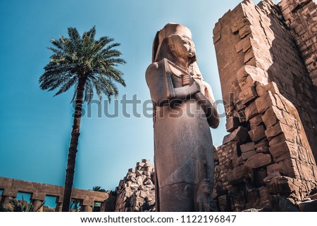 A statue standing tall at the entrance of  some ancient buildings