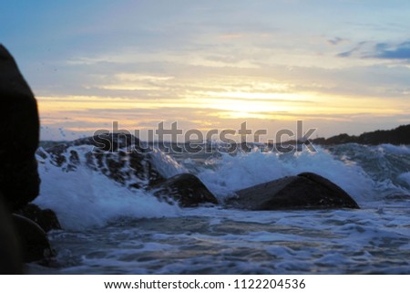 Sea waves blowing rocks at the beach at sunset.