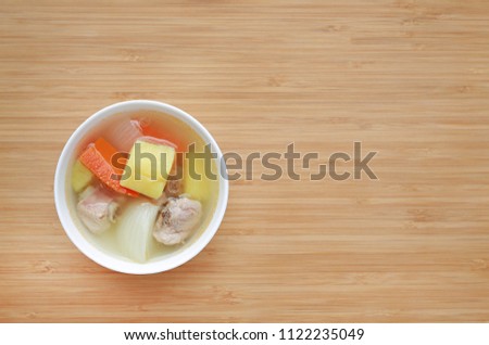 Bowl of pork bone soup with carrot, onion and potato on wood board background.