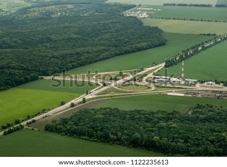 Aerial view of a green field, cultivated land. Intercity roads. Red car on the road. Country road viaduct. Concrete road curve of viaduct. Road traffic in city.