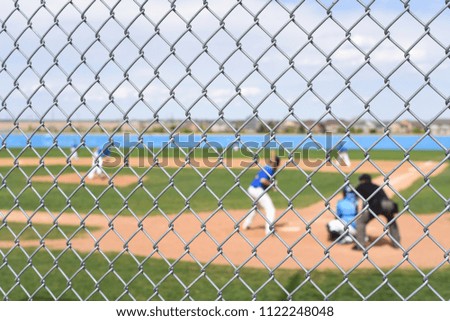 Picture of baseball players playing a game on a baseball diamond in the summer behind a chain link fence background