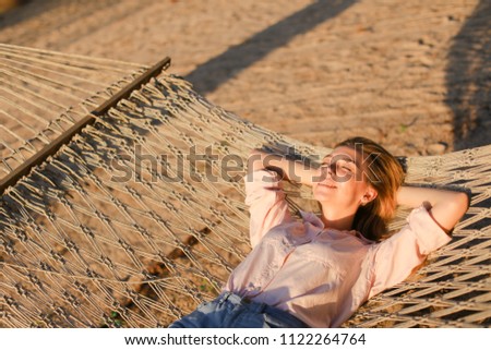 Young caucasian blonde girl wearing jeans shorts and lying on sand in wicker barefoot. Concept of summer vacations and resting on beach.