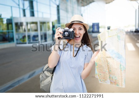 Young surprised traveler tourist woman take pictures on retro vintage photo camera, hold paper map at international airport. Female passenger traveling abroad on weekends getaway. Air flight concept