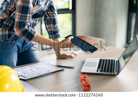 Woman civil architect engineer choose color from palette with laptop on wood table.Engineer and architecture concept.Blue print is fake only for stock photo.