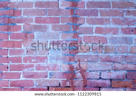 Close up view of an antique distressed brick wall with colorful pink to purple color bricks that are severely weathered and cracked