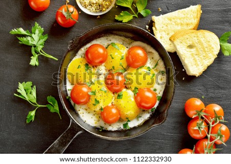 Fried eggs with tomatoes in frying pan on black stone background. Top view, flat lay
