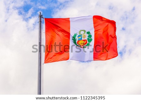 The national flag of Peru flutters in the wind against a blue cloudy sky.