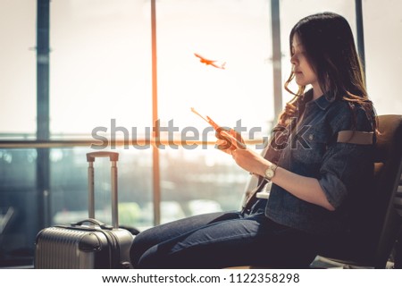 Beauty Asian woman with suitcase luggage waiting for departure while using smart phone in airport lounge. Female traveler and tourist theme. High season and vacation concept. Airplane background