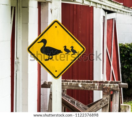 Crossing ducks sign posted on a wooden beam next to a red barn.