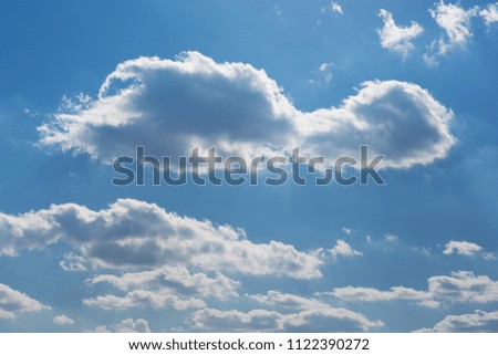 many large clouds in the backlight, stretching into the distance in perspective, against the blue sky