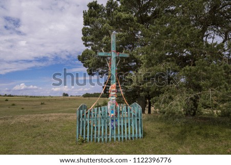 Old wooden cross at country road. Green grass and blue sky.