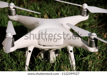 White quadcopter Drone with 4K digital camera on grass is ready for take off to fly in air to take photos, record footage from above. Drone with four motors, propellers, camera and red warning lights.