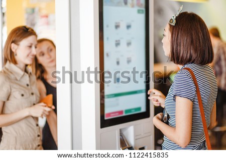 Group of people, friends ordering food at the touch screen self service terminal by the electronic menu in the fastfood restaurant Royalty-Free Stock Photo #1122415835