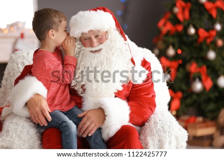 Little boy whispering in authentic Santa Claus' ear indoors