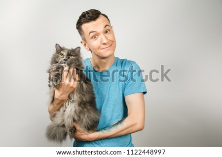 Young guy holds gray Britain cat on light gray background.