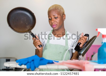 young beautiful sad and depressed afro American black woman with cooking pan and iron working stressed and tired at home kitchen overworked cleaning and washing in domestic work stress