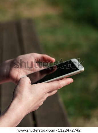 Woman holding smartphone cellular close up outdoors park green background. Female hands typing mobile phone touch screen device gadget. Technology communication concept copy space