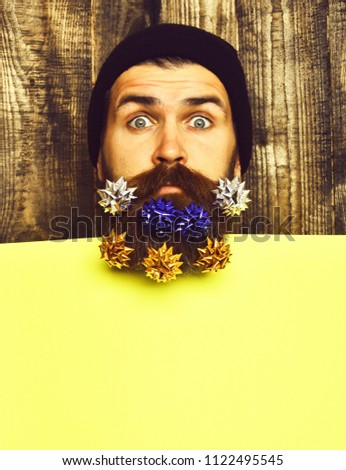 Bearded man, long beard. Brutal caucasian surprised hipster with colorful gift decoration stars in moustache, yellow paper sheet on brown wooden vintage studio background