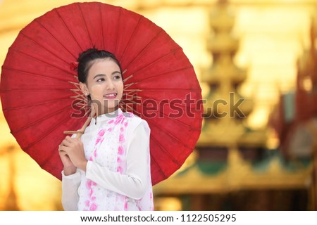 Burmese woman holding a red umbrella walking at Shwedagon Pagoda. Young Myanmar girls with Thanaka, a yellowish-white paste made from ground bark and used as a cosmetic and for sunburn.