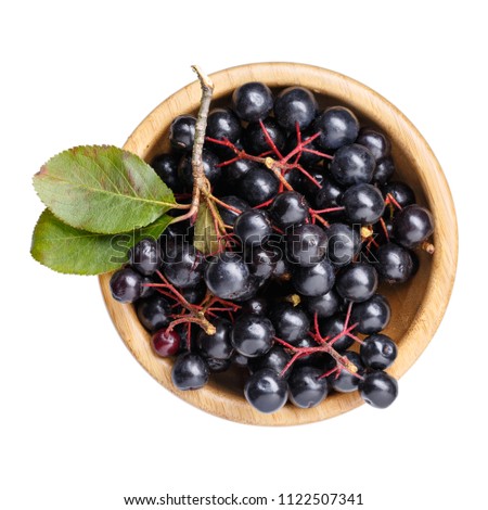 Black chokeberry berries ( Aronia melanocarpa ) in wooden bowl isolated on white. Top view. Royalty-Free Stock Photo #1122507341