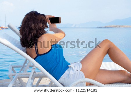 A girl on a lounge takes pictures of a beach and a bay on her mobile phone. A Turkish woman is resting in the resort of Bodrum.