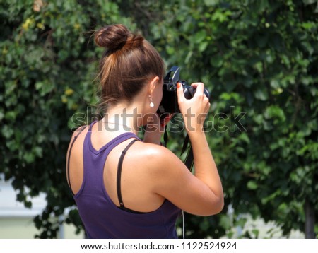 Young woman with a SLR camera in her hands, rear view. Girl photographing on background of summer trees in sunny day 