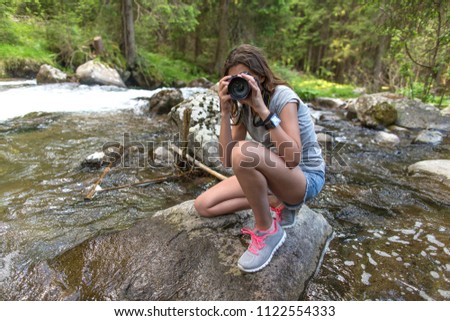 A young girl takes pictures of a mountain river. A teenager with a camera. The child is a photographer. Moena, Trentino Alto Adige, the Alps in summer. Mountain river in the Alps.
