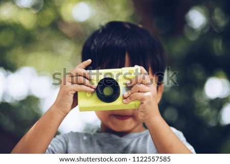 Asian child takes photo with toy camera on nature green bokeh background