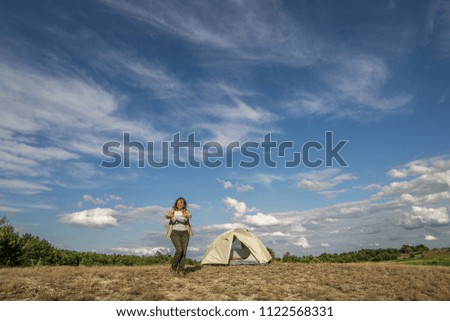 The girl is sitting near the tent. A smiling brunette is resting in nature. Camping in the background of a blue cloudy sky.Selfie.