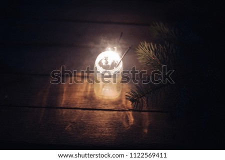 Bengal light in a glass jar on a wooden background with branches of a Christmas tree.