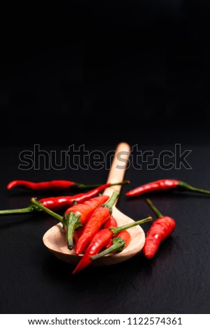 Red Thai chilies pepper in wood spoon on black slate stone background