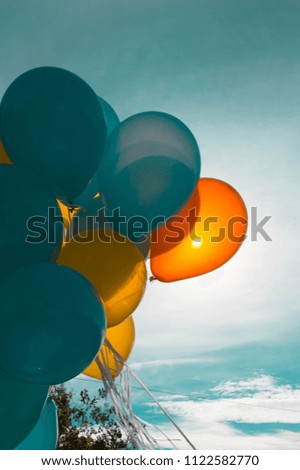 Colorful turquoise and bright yellow helium balloons with the sun on the sky as background celebrating a holiday 