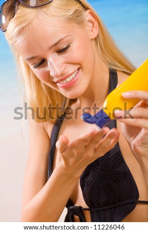 Young happy smiling woman with sun-protection cream on beach. Focus on woman.
