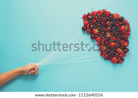 Hand holding balloons made of berries on blue paper background. Healthy eating concept. Flat lay. Toned Royalty-Free Stock Photo #1122640556